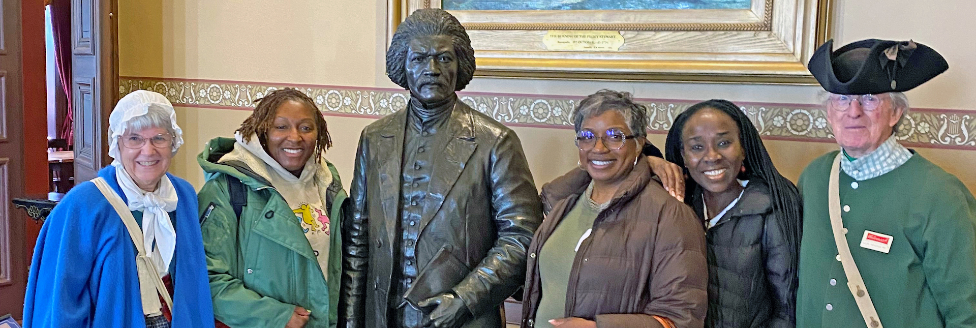 Group on walking tour with period-attired guides next to Frederick Douglass statue.